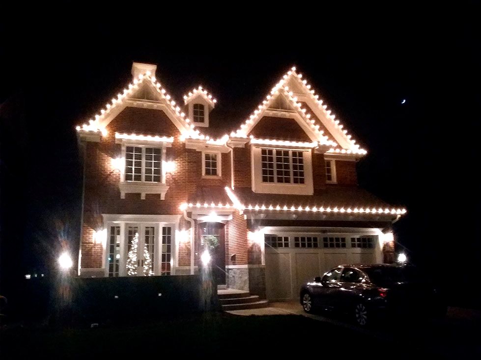 Glowing warm white LED light string along the dormers of a ranch house