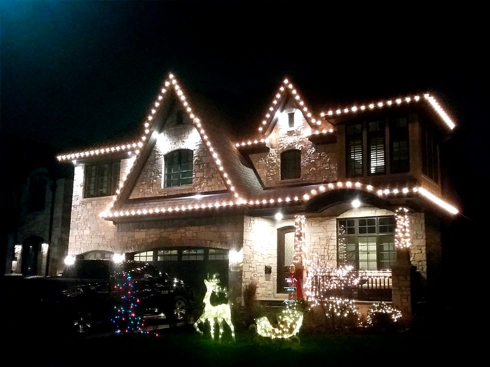 Suburban home with warm yellow holiday lights reflecting off pristine snow